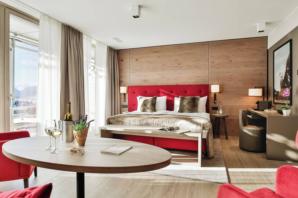 Ein Hotelzimmer mit Bett, Schreibtisch, Stuhl, rundem Tisch und Blick auf die Berge.