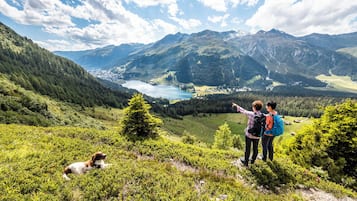 Eine Berglandschaft mit einem See, einem Hund und zwei Wanderern.
