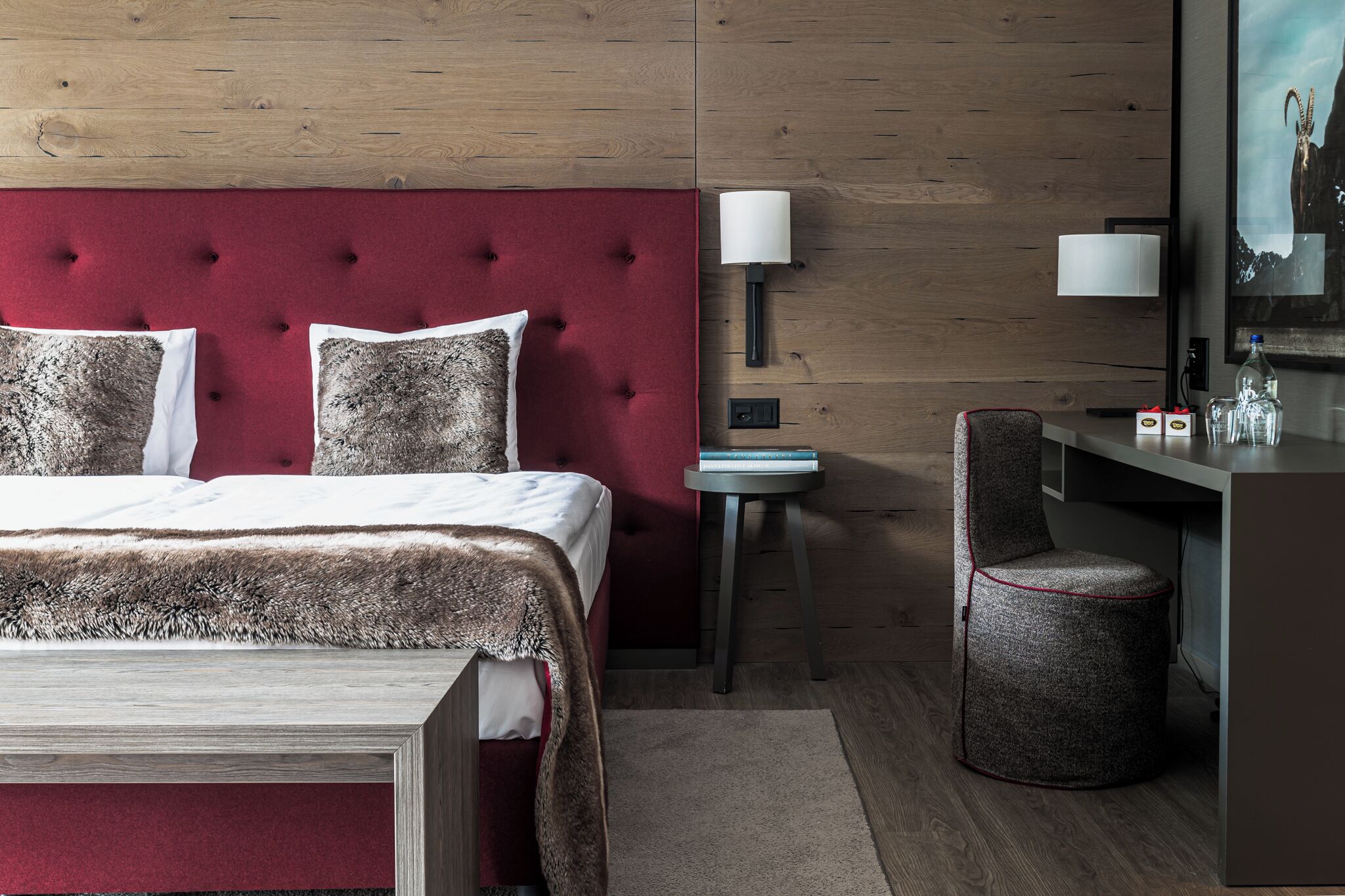 Una habitación de hotel moderna con un cabecero tapizado rojo, una mesita auxiliar pequeña, un sillón tapizado de color gris y un espejo grande.