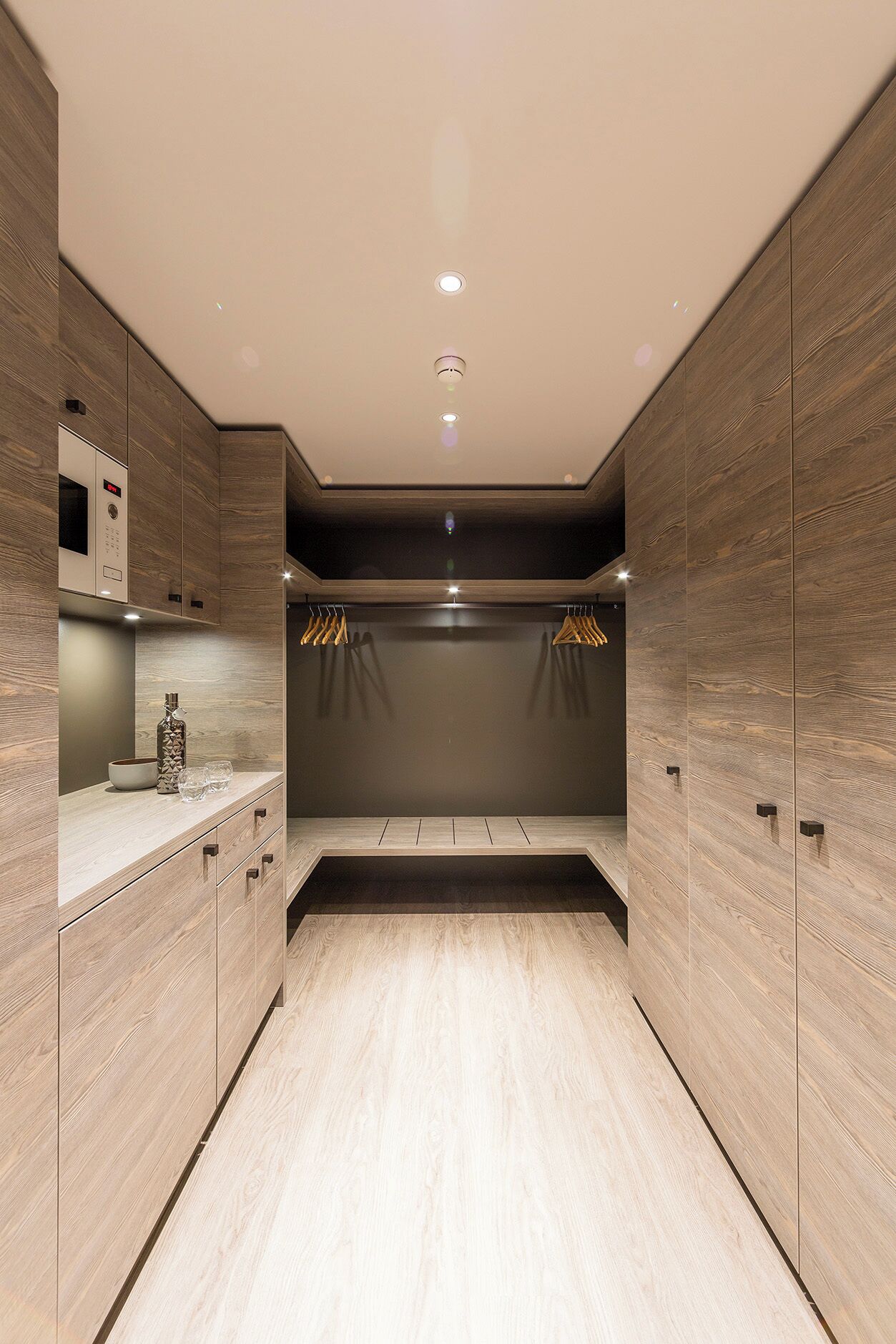 A modern, minimalist room with wooden paneling, a built-in wardrobe, a small kitchen area, and a seating area with a bench.