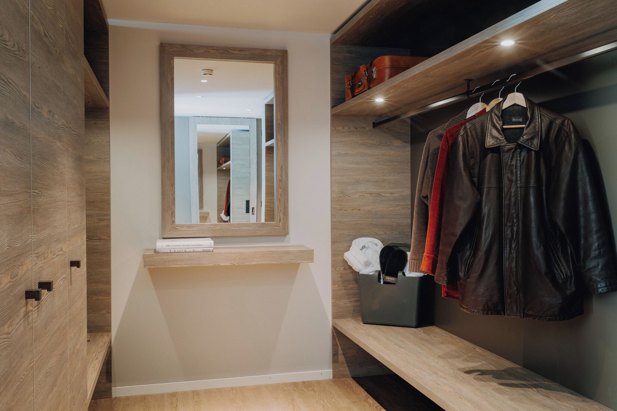 A modern bathroom with a mirror, wooden vanity, and a hanging coat rack.