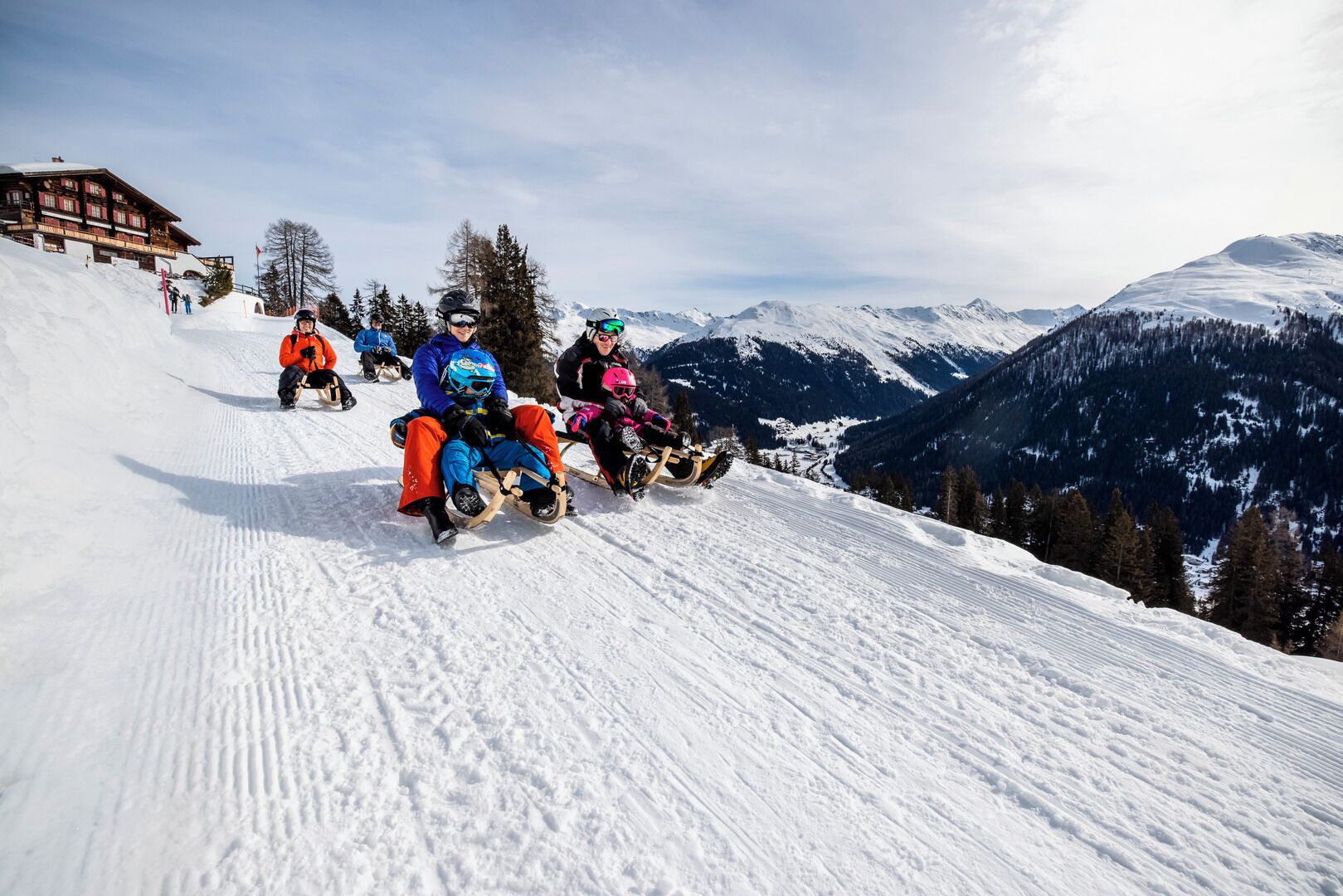A group of people sledding down a snowy slope with a mountain view in the background.