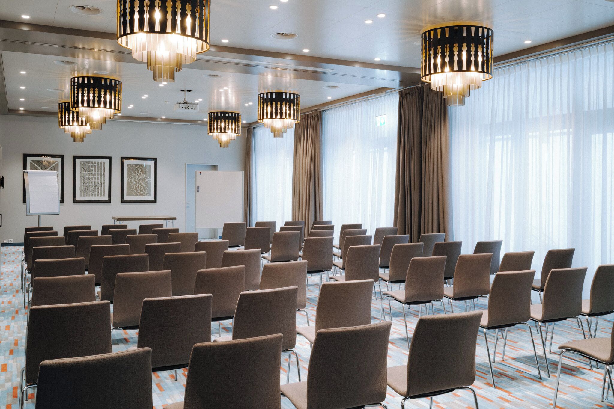 Ett konferensrum med rader av stolar, stora fönster med gardiner och kristallkronor.