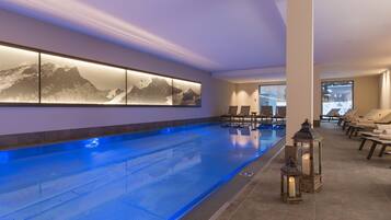 Relax by the serene indoor pool, surrounded by lounge chairs and a modern artwork.