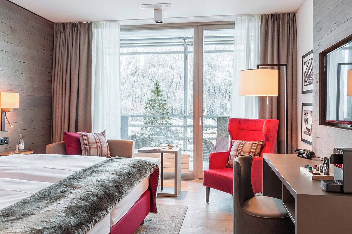 Ein Hotelzimmer mit Bett, Schreibtisch, Stuhl und Blick auf eine verschneite Landschaft.