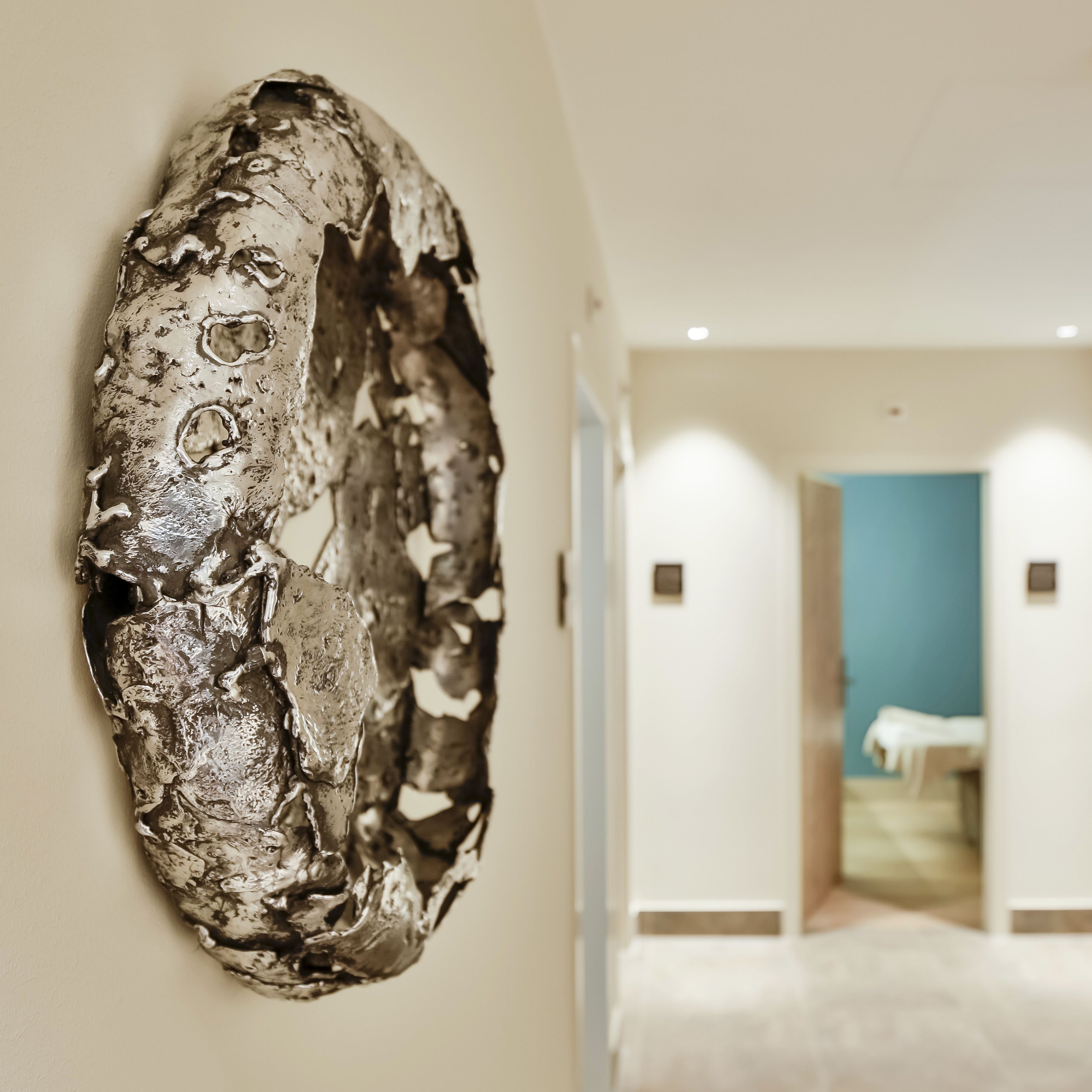 Ein Flur mit einer großen, abstrakten Skulptur an der Wand, einem Bett im Hintergrund und einer blauen Akzentwand.