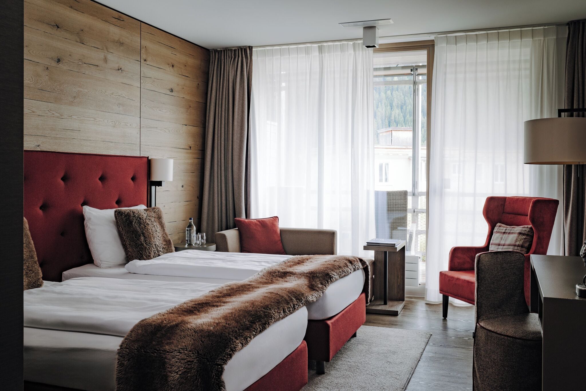 A hotel room with a large bed, a desk, a chair, and a view of the outdoors.