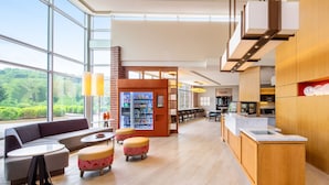 A modern hotel lobby with a large seating area, a refreshment bar, and a view of the outdoors.