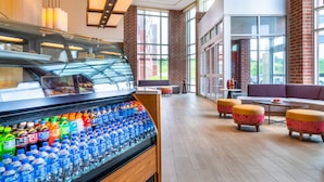 A modern hotel lobby with a refrigerated beverage display, seating area, and large windows.
