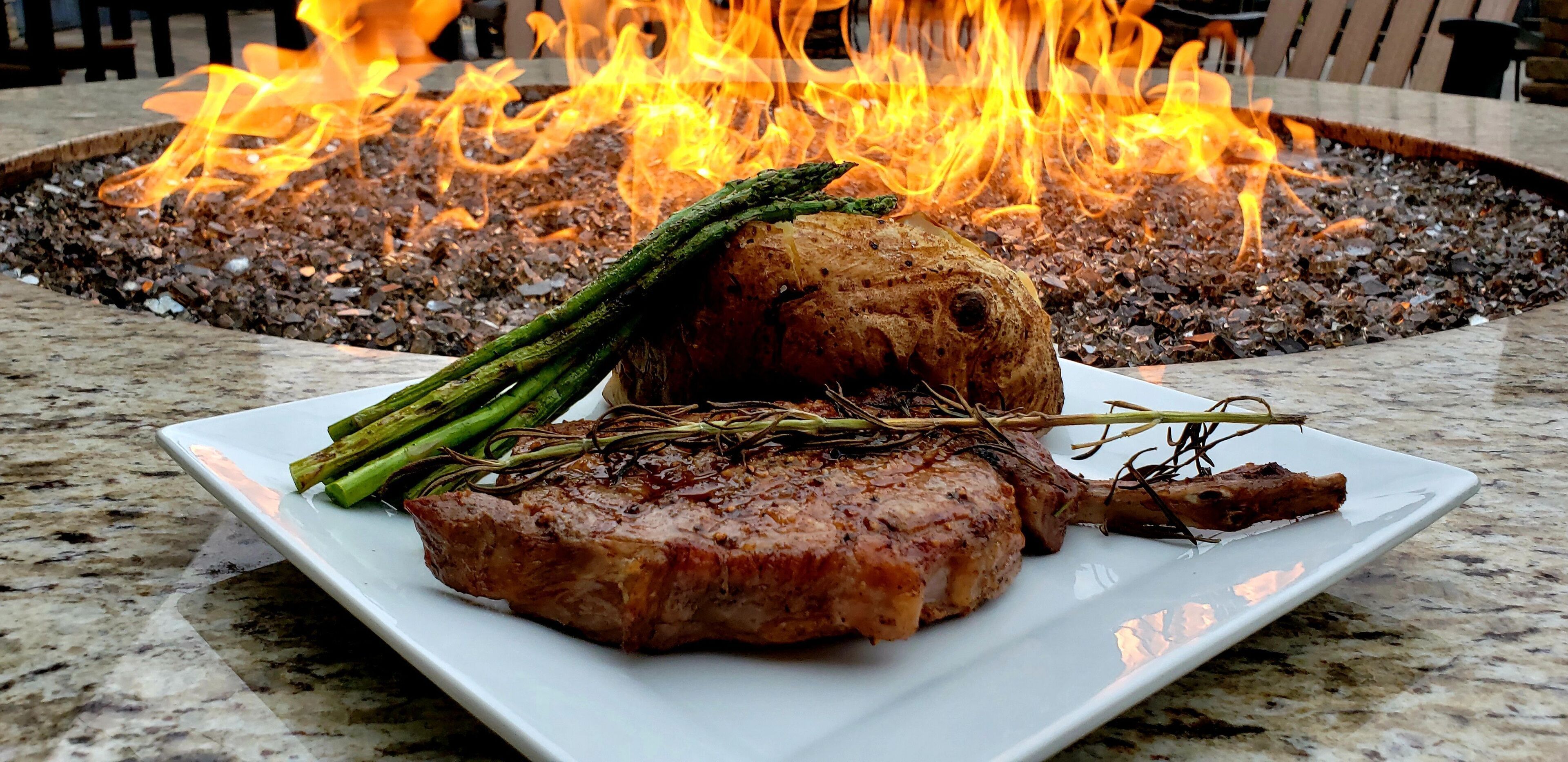 Ein Teller mit Steak und Spargel auf einer Marmorplatte, im Hintergrund ein Feuerkorb.