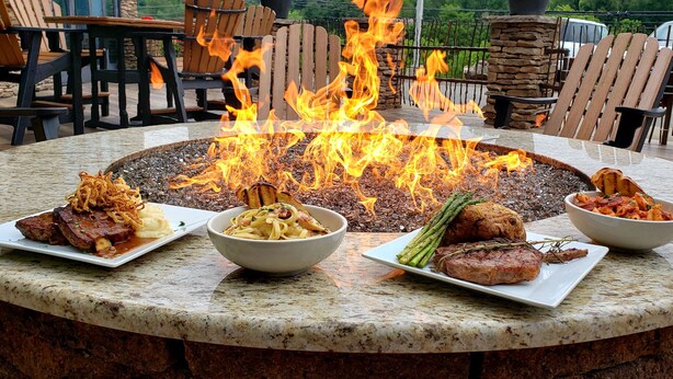 A round outdoor dining table with a fire pit in the center surrounded by chairs.