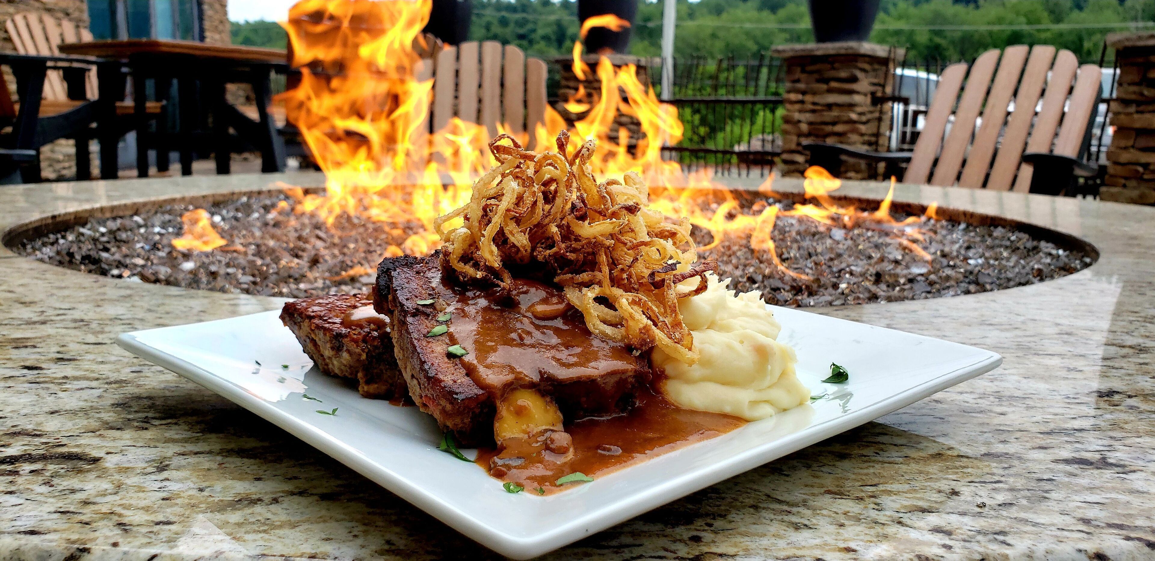 A plate of food with a fire pit in the background.