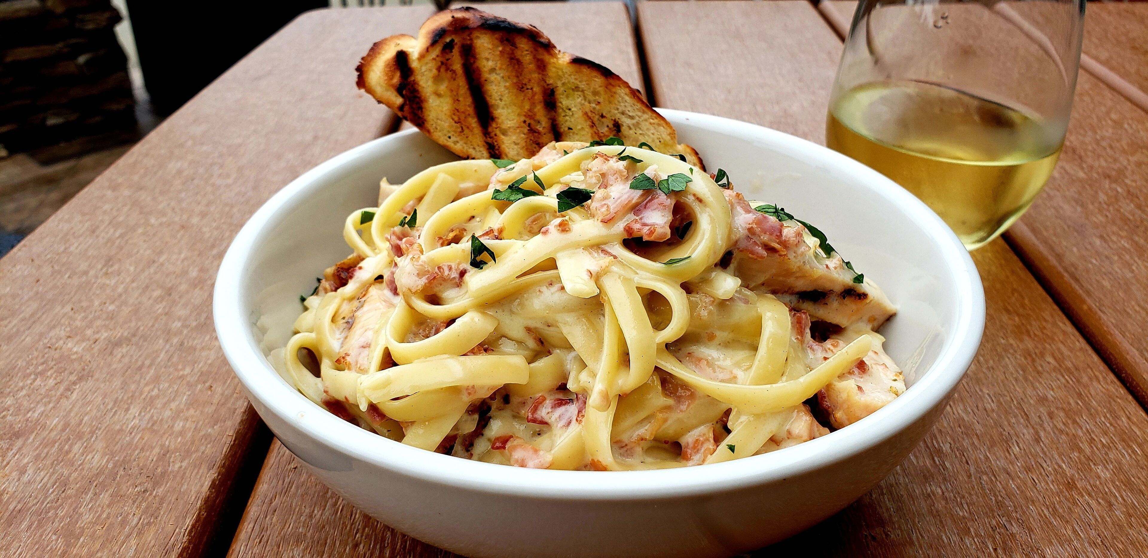 A bowl of pasta with a slice of toasted bread on a wooden table.