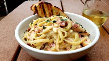 A bowl of pasta with a slice of toasted bread on a wooden table.