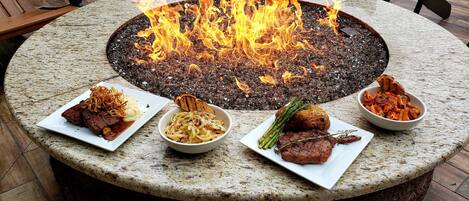 A round table with a fire pit in the center surrounded by four plates of food.