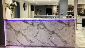 A marble reception desk with a purple LED light strip, a clock, and a vase with flowers. - Hôtel Les Beaux Soleils (Osny)