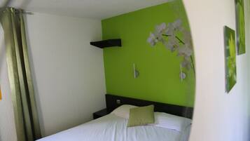 A single bed with white bedding, a green accent wall, and a white orchid decoration.