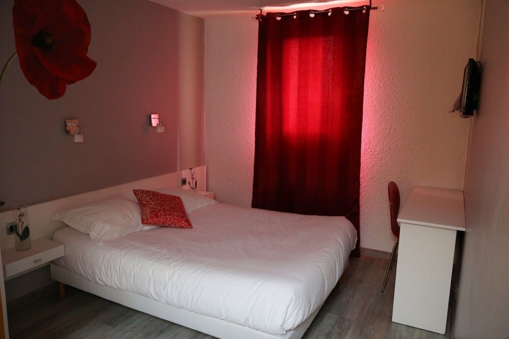 A bedroom with a bed, a bedside table, a red curtain, and a small white cabinet.
