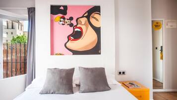 A bedroom with a large bed, two pillows, a painting, and a window with a view of buildings.