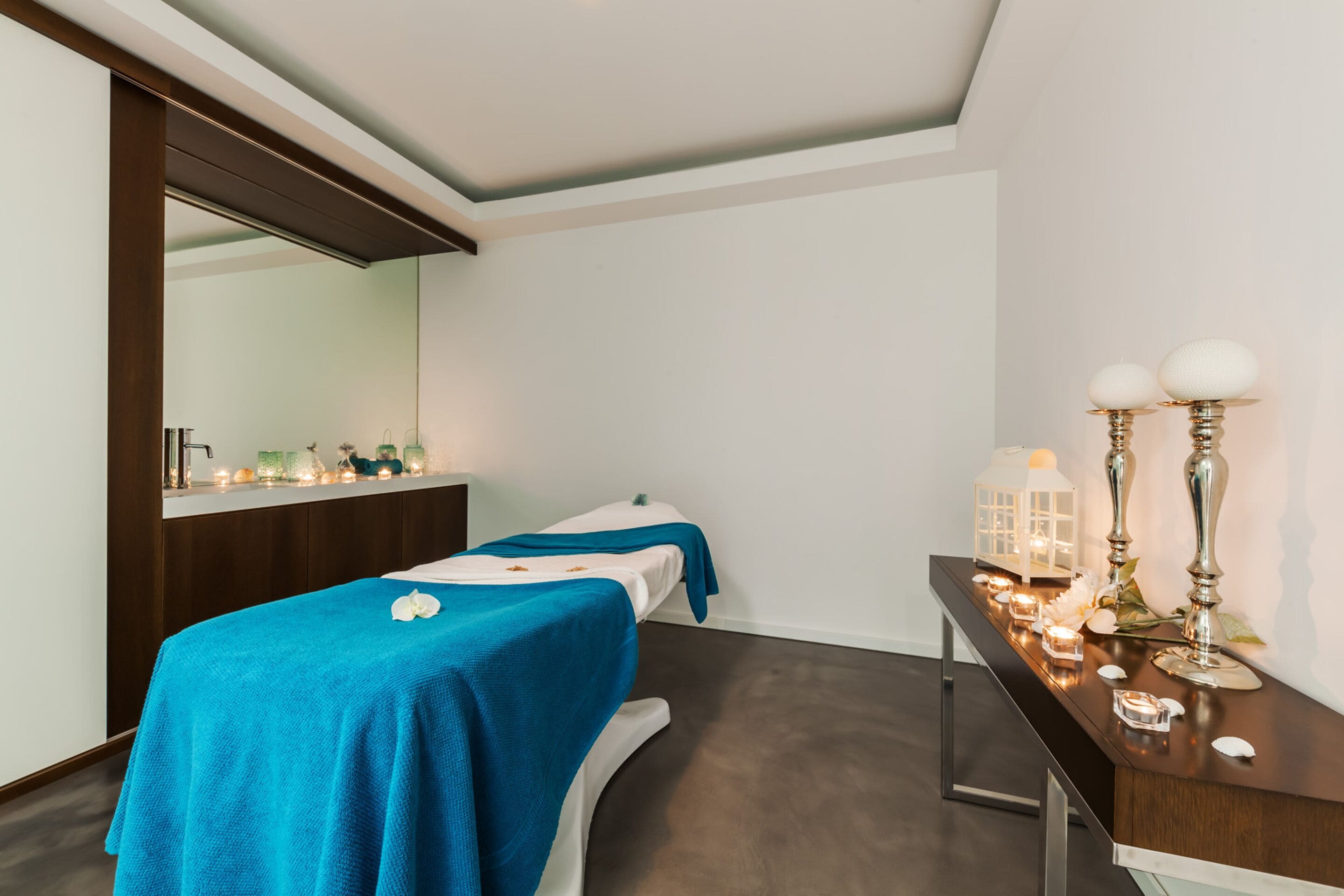 A room with a bed, a mirror, a vanity with candles, and a small table.