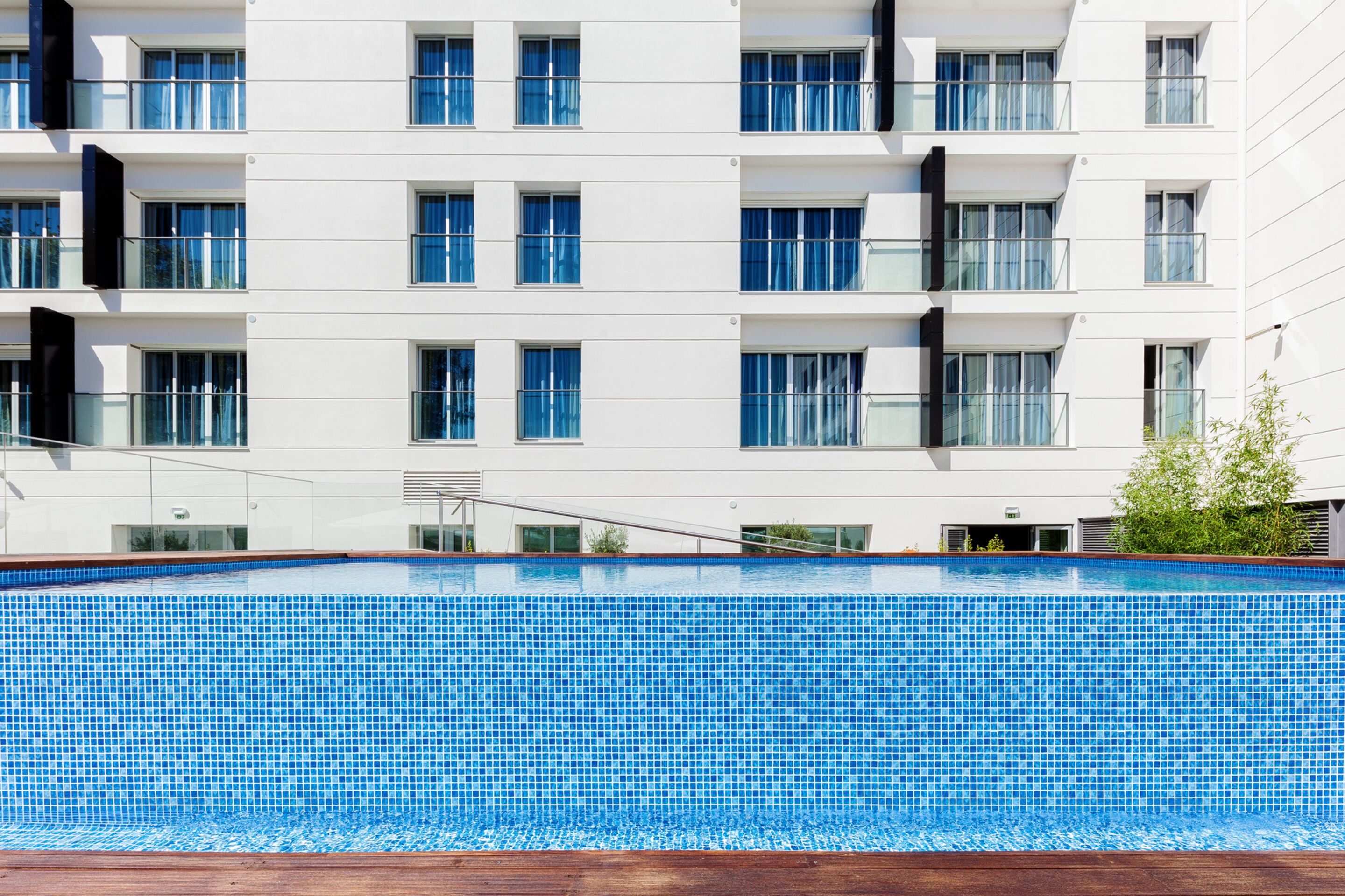 Un hotel moderno con una piscina grande, varios balcones y una fachada blanca y limpia.
