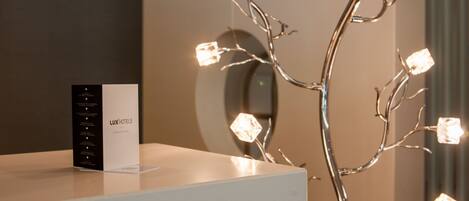 A reception desk with a black and white brochure for LUXHOTELS and a decorative metal sculpture with illuminated cubes.