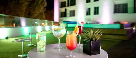 Una mesa con tres bebidas, una planta en maceta y un edificio al fondo.