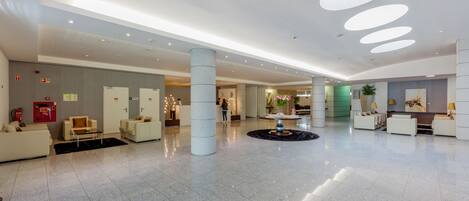 A spacious lobby with a polished tile floor, several seating areas, and a central decorative fountain.