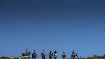 Um grupo de pessoas cavalga em uma encosta rochosa sob um céu azul límpido.