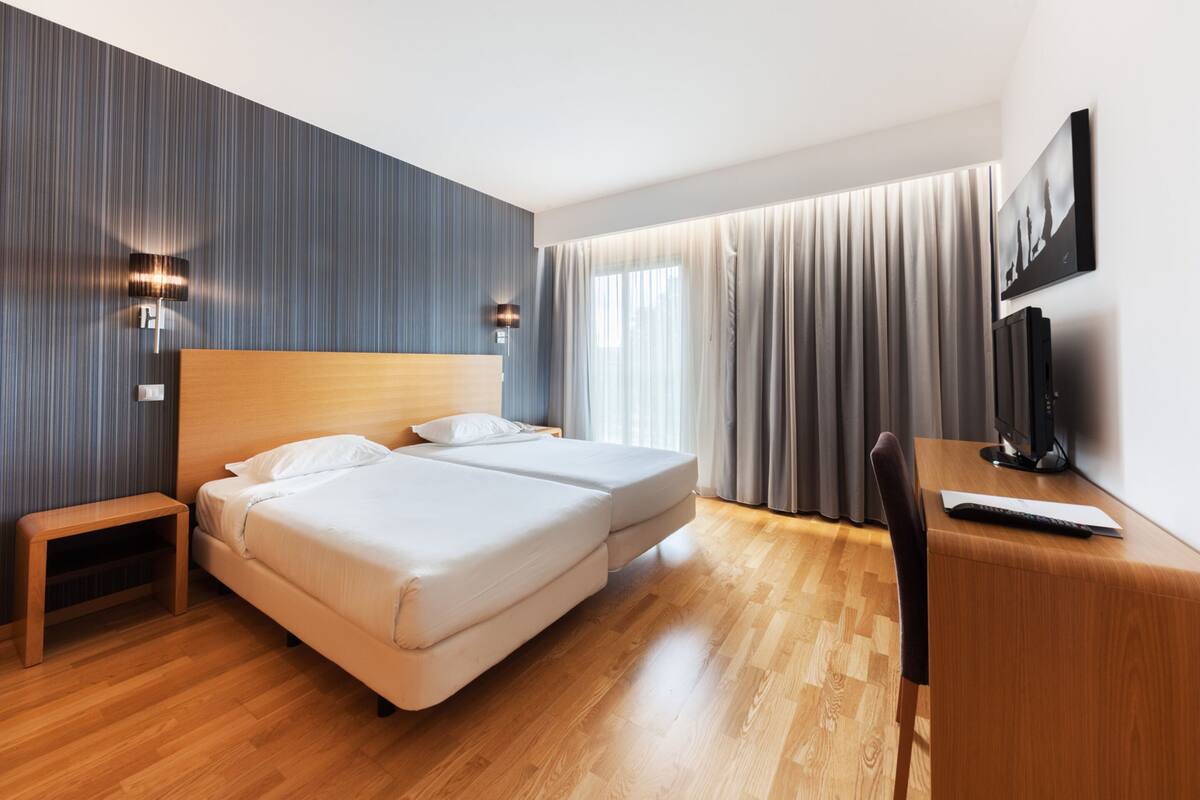 Une chambre d’hôtel moderne avec deux lits, un bureau en bois, une télévision et une œuvre d’art accrochée au mur.