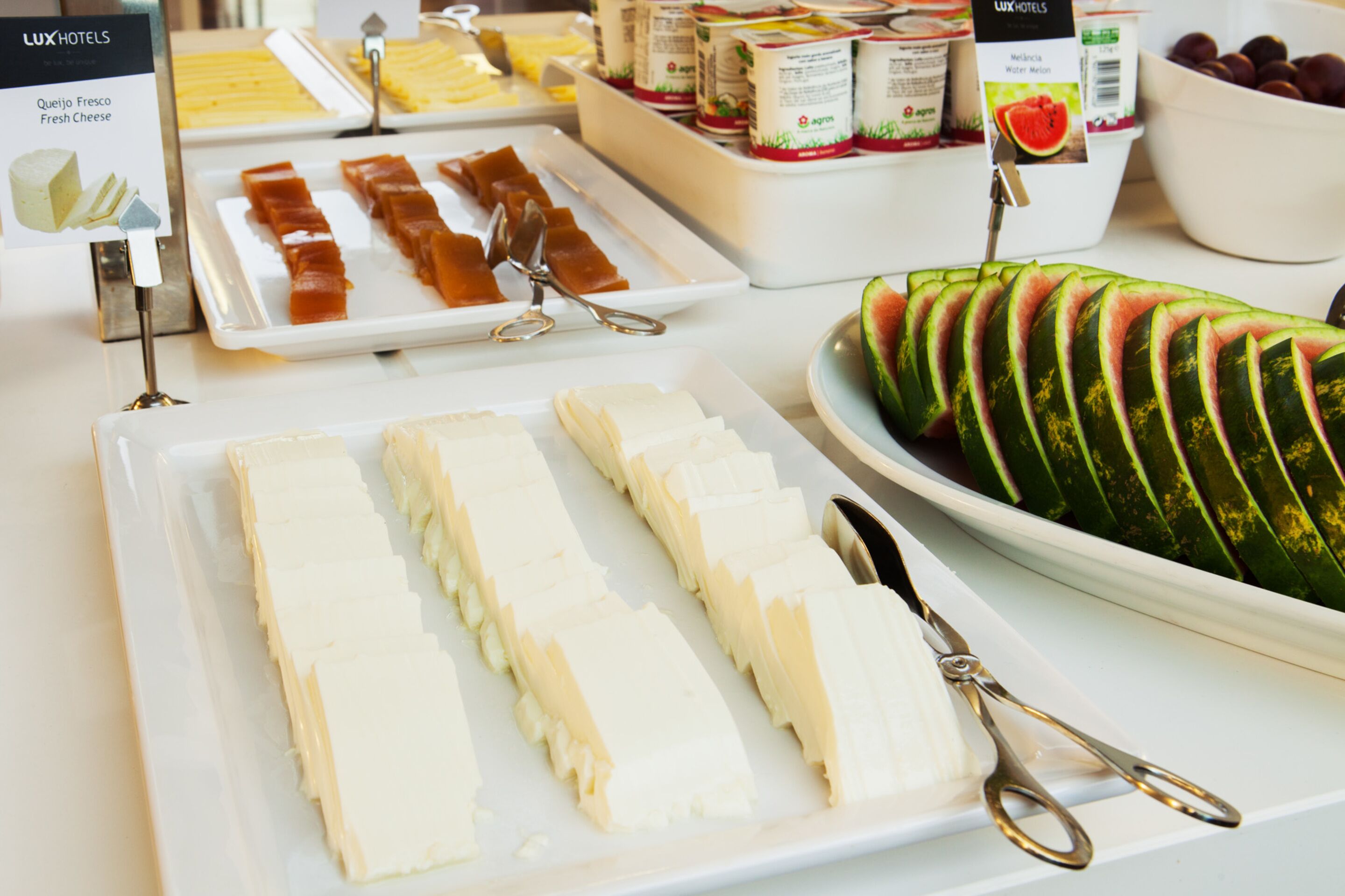 Un bufé con diversos alimentos, incluyendo queso fresco, mermeladas y sandía en rodajas.
