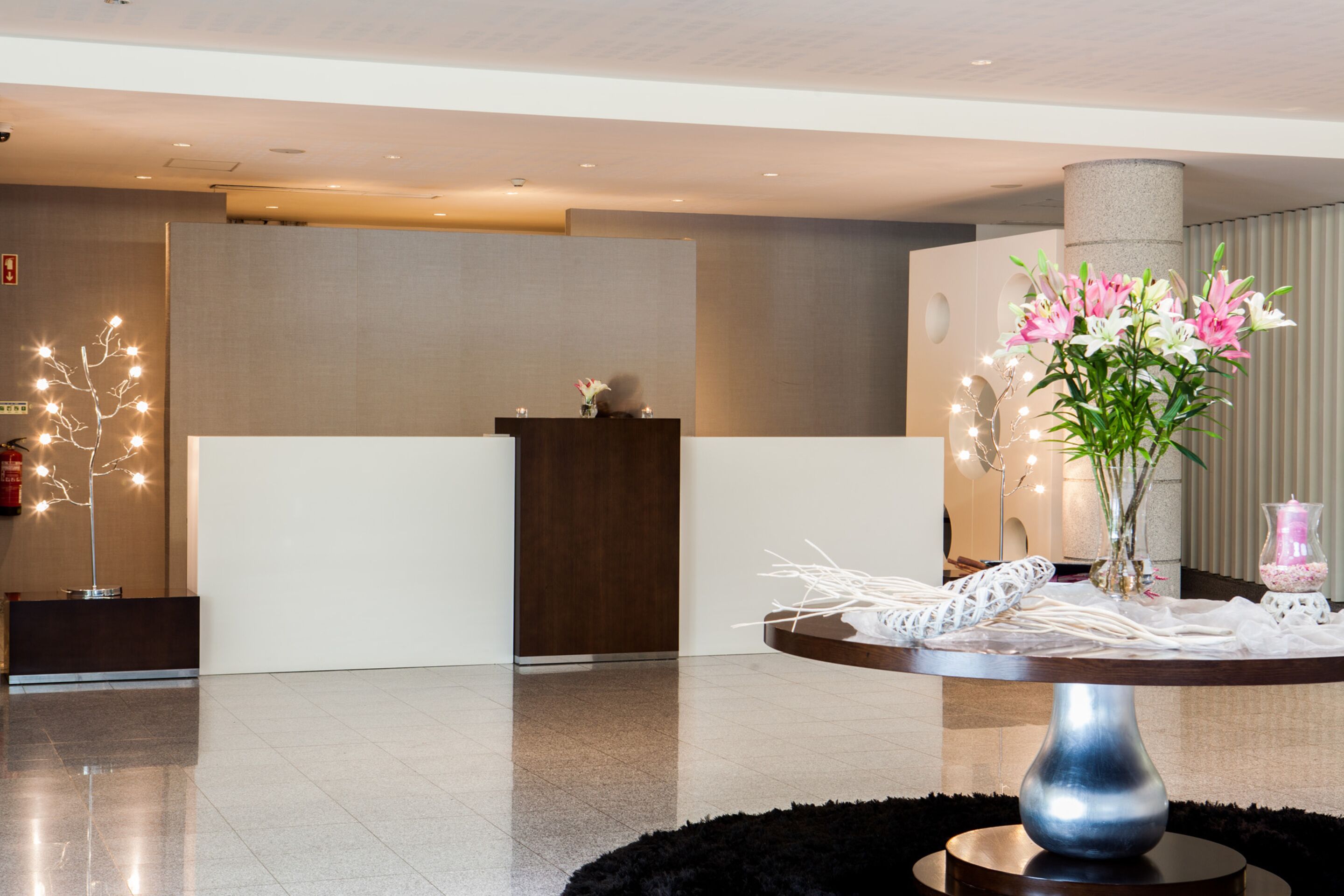 Un hall d’entrée moderne avec un comptoir d’accueil, un vase décoratif rempli de fleurs et un luminaire original fixé au mur.