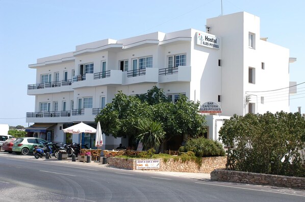 A white multi-story building with balconies, a sign for 'Hostal Illes Pitiues', and a 'BAR CAFETERIA Illes Pitiues' sign. - Hostal Illes Pitiüses (Formentera)
