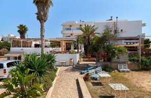 A courtyard with outdoor seating, palm trees, and a white building with multiple floors. - Hostal Illes Pitiüses (Formentera)