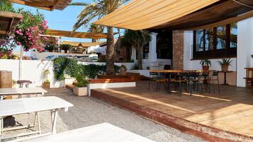 An outdoor patio area with wooden tables and chairs, surrounded by potted plants and a stone wall.