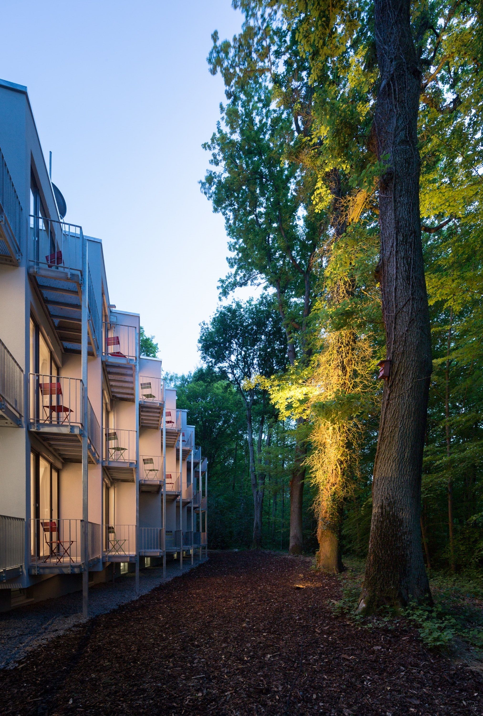 A row of modern buildings with balconies, surrounded by a forested area.