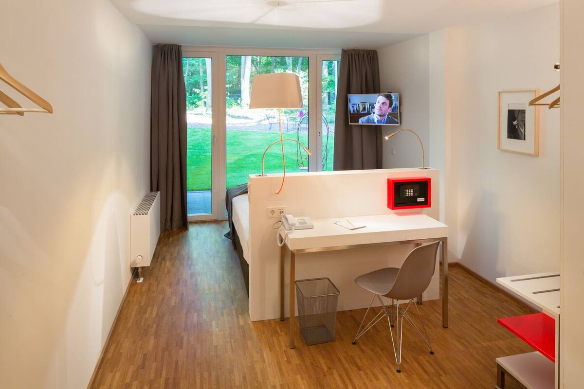 A hotel room with a desk, chair, TV, and a view of the outdoors.