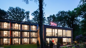 A modern hotel with a glass facade, a visible restaurant area, and a well-maintained garden. - V-Hotel (Bonn)