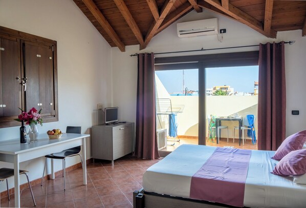 A bedroom with a bed, a desk with a computer, a TV, and a view of the outside.