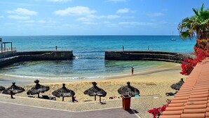 A beach with thatched umbrellas, a sandy shore, and a clear blue sky.