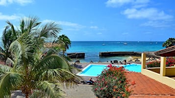 Ein Poolbereich mit Blick auf das Meer und Boote, umgeben von Palmen und einem Ziegeldach.