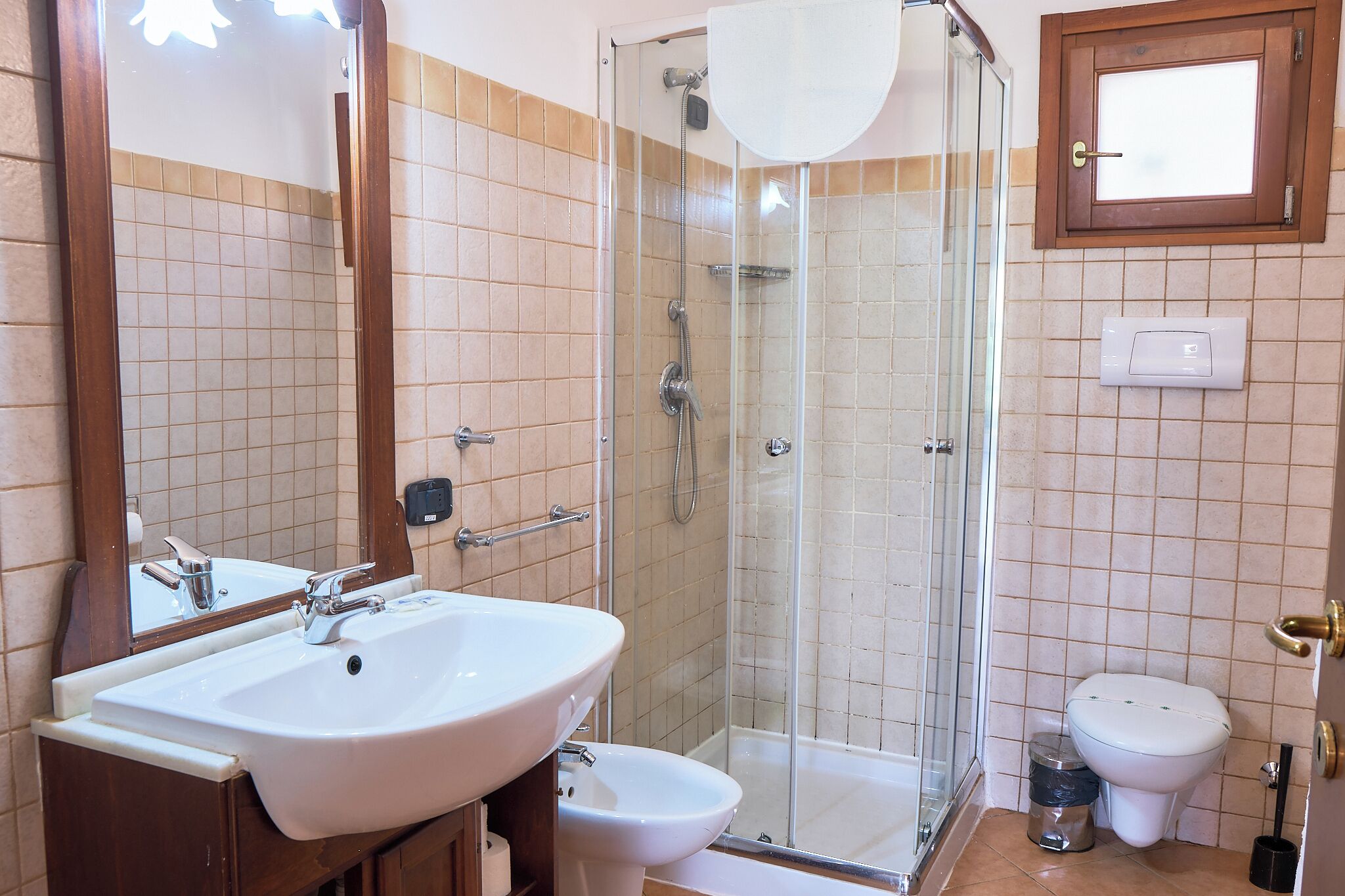 A bathroom with a glass-enclosed shower, a white sink, a bidet, and a toilet.
