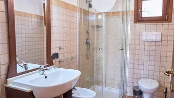 A bathroom with a glass-enclosed shower, a white sink, a bidet, and a toilet.