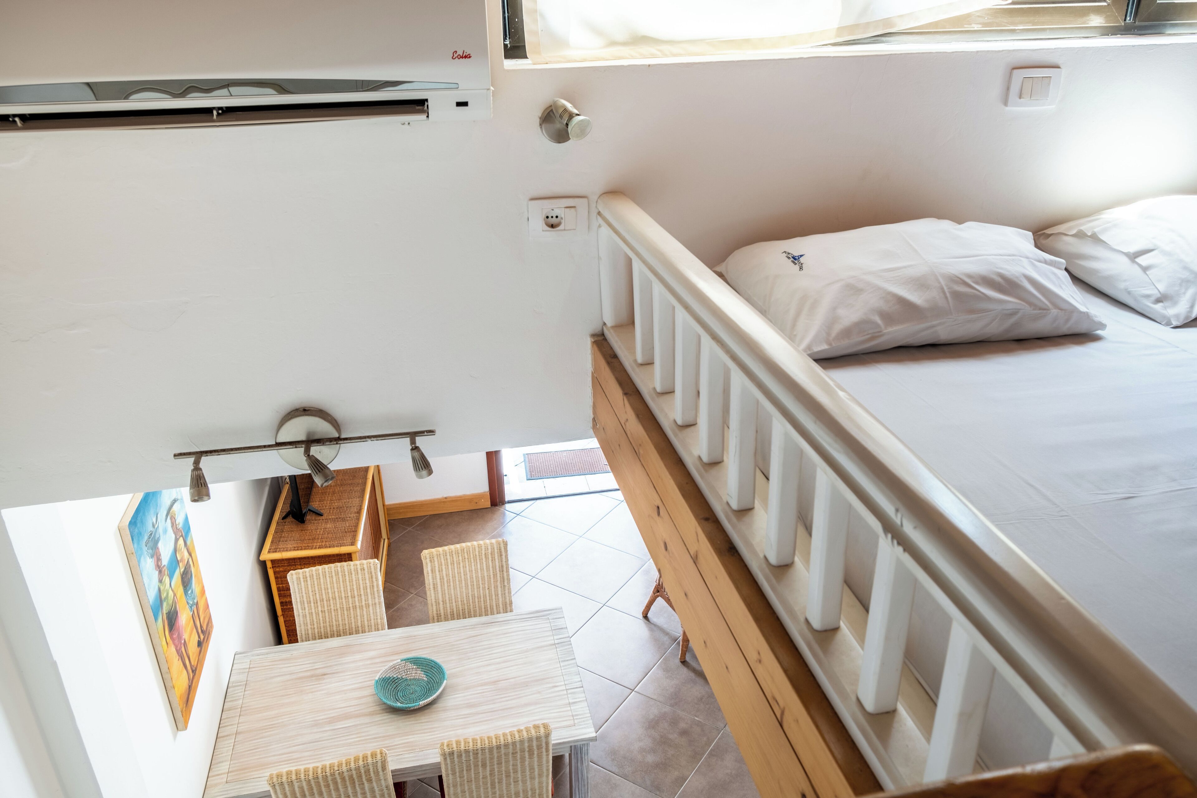 A bedroom with a bed, a small table with chairs, a painting, and a window.