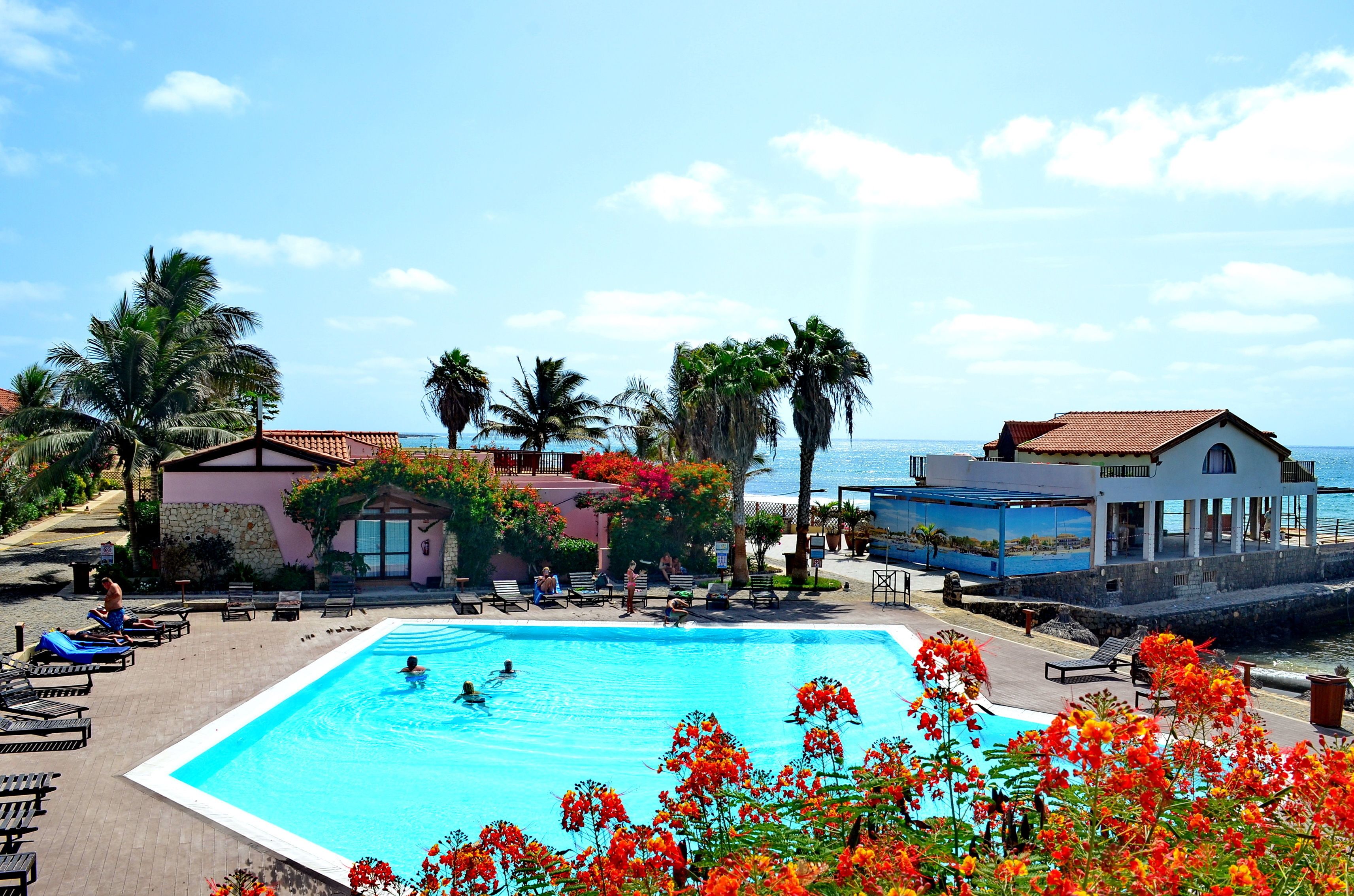 A pool area with lounge chairs, a swimming pool, and a view of the ocean.