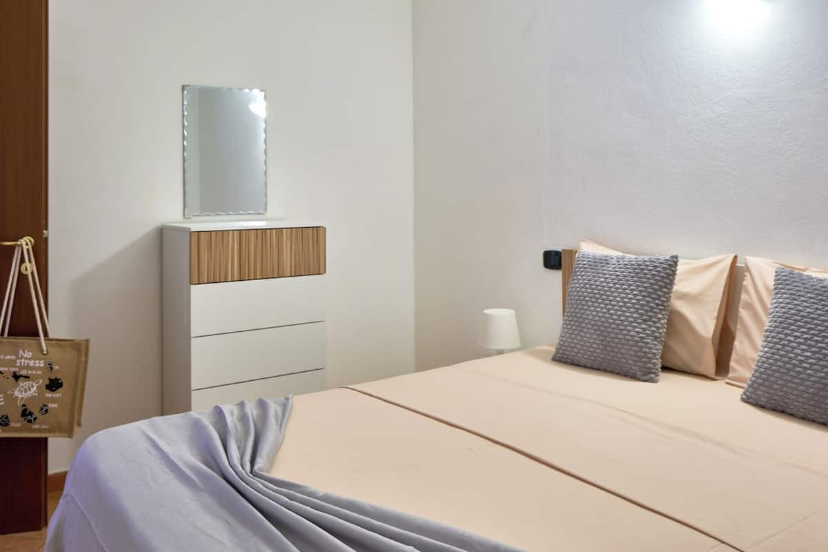 A bedroom with a bed, a dresser with a mirror, and a bedside table with a lamp.
