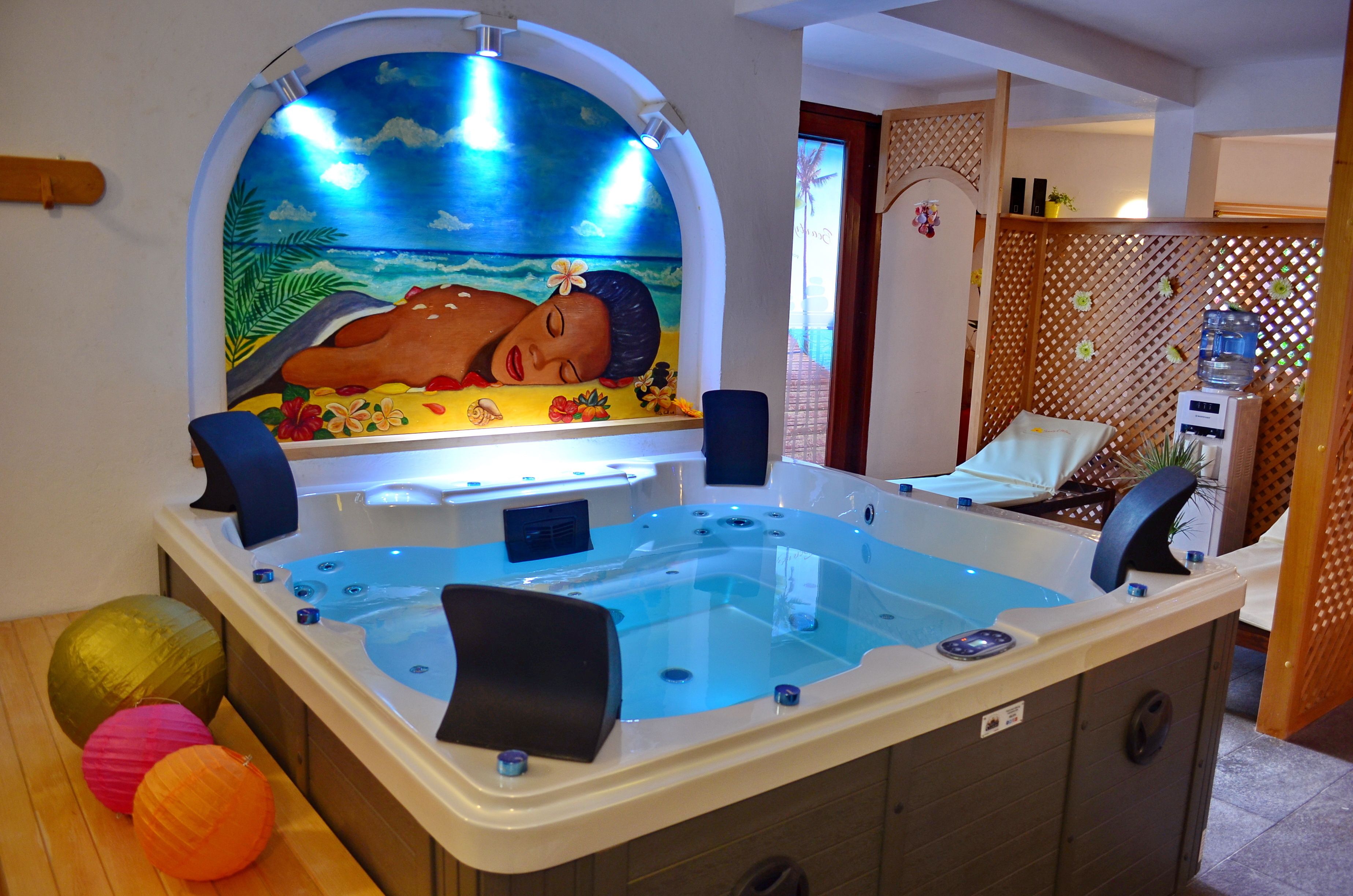 Un cuarto de spa con hidromasaje, un mural de paisaje tropical y piso de madera.