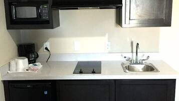 A compact kitchen with dark cabinets, a microwave, a coffee maker, a sink, and a dishwasher.