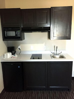 A compact kitchen with dark cabinets, a microwave, a coffee maker, a sink, and a dishwasher.