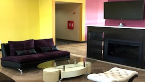 A modern living room with a purple sofa, a glass coffee table, and a white ottoman. - Residency Suites - Cotulla (Cotulla)